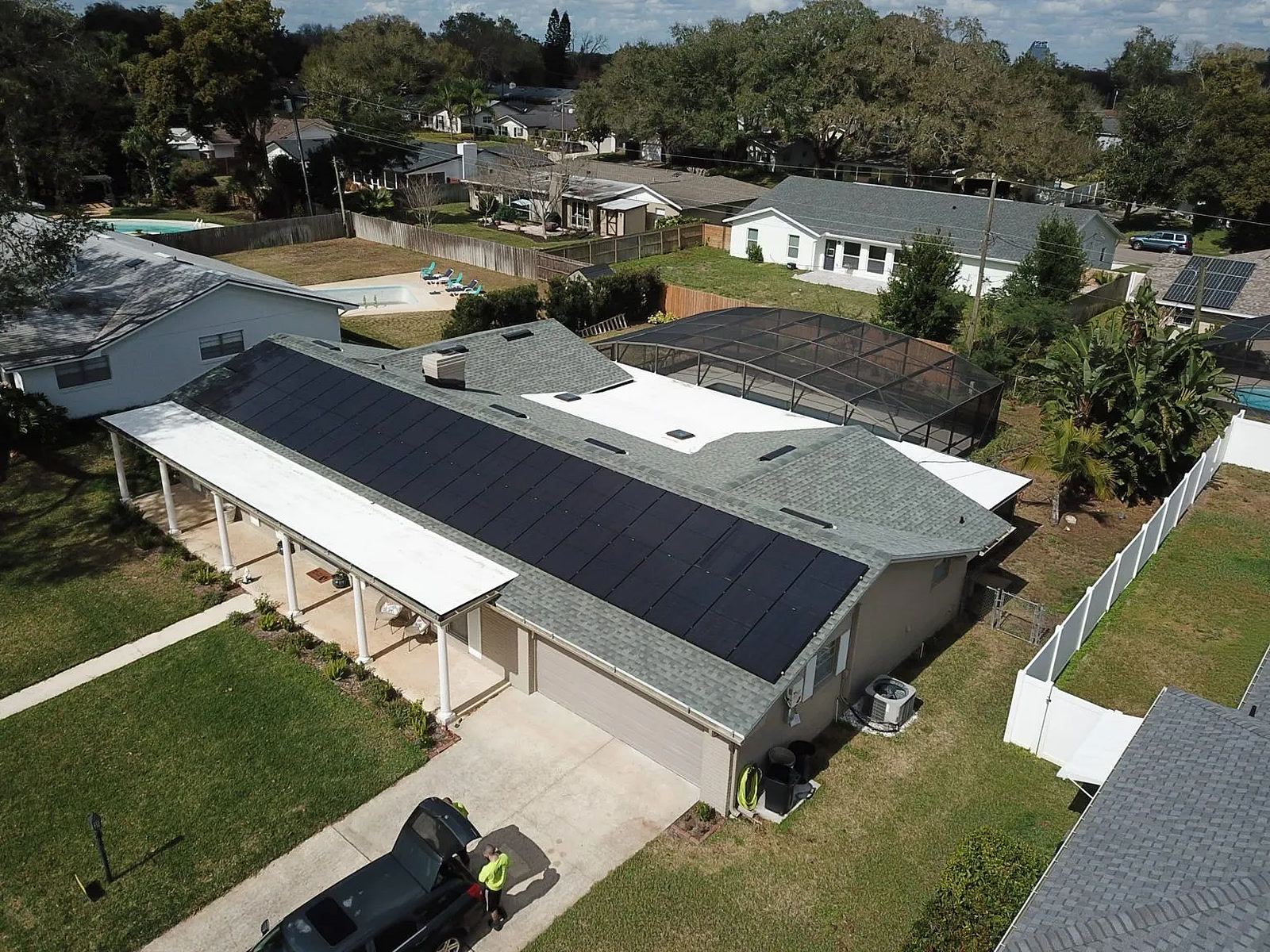 Aerial view of a solar array on a carport roof over a pool deck with palm trees