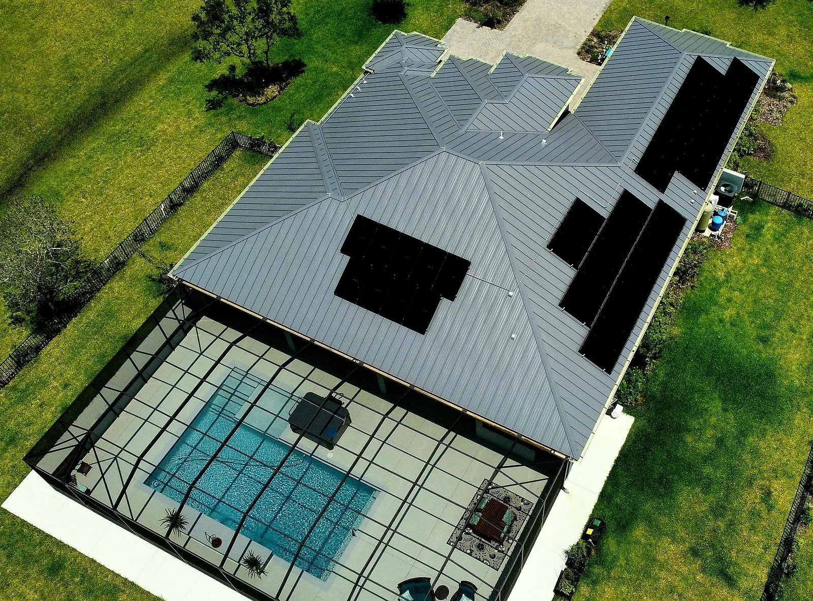 Aerial view of a standing-seam metal roof solar array over a home with a screened pool